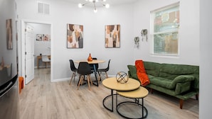 A modern living room with a green sofa, a round coffee table, and a dining area with a white table and chairs. - Mojitos - Springfield Brand NEW Apt! (Jacksonville)