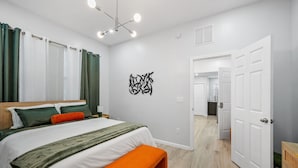 A modern bedroom with a bed, a bench, a wall art piece, and a door leading to another room. - Mojitos - Springfield Brand NEW Apt! (Jacksonville)