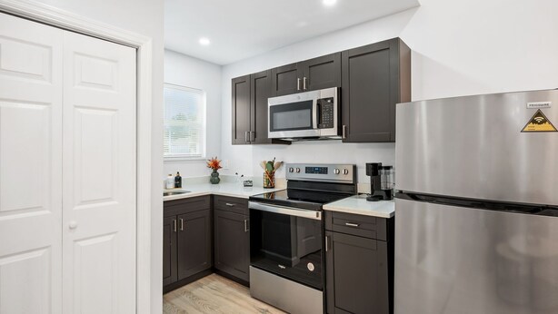 A modern kitchen with dark cabinets, stainless steel appliances, and a white countertop. - Mojitos - Springfield Brand NEW Apt! (Jacksonville)