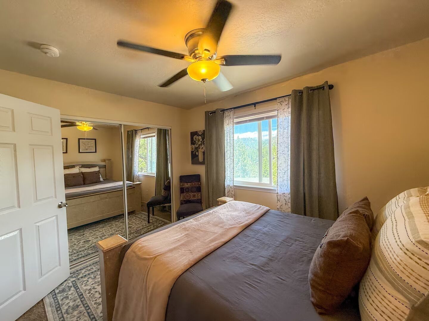 A bedroom with a bed, a ceiling fan, a window with curtains, and a door.