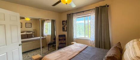 A bedroom with a bed, a ceiling fan, a window with curtains, and a door.