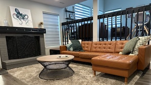 A modern living room with a brown leather sofa, a round coffee table, and a fireplace. - Family Retreat, Fire Pit • EV Charger • Near Denver • Sleeps 9 (Arvada)