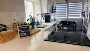 A modern kitchen with white cabinets, a black countertop, and a sign that reads "WELCOME! WIFI, BANNY & THE JETS PASSWORD 305!". - Family Retreat, Fire Pit • EV Charger • Near Denver • Sleeps 9 (Arvada)