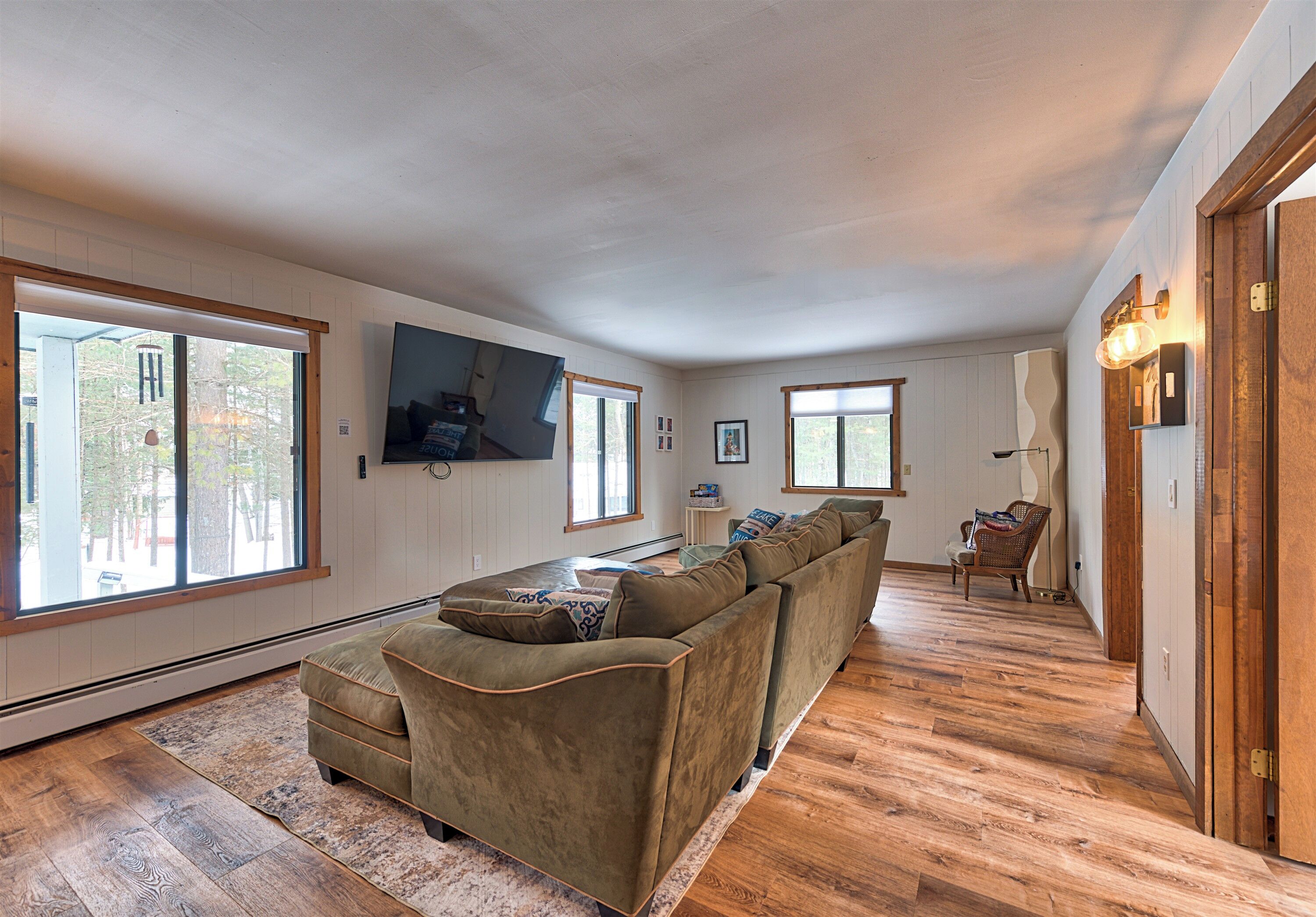 Un salon spacieux avec un grand canapé d’angle, un téléviseur à écran plat fixé au mur et un plancher en bois.