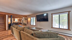 Un saló d'estar espaiós amb un sofà modular gran, una televisió de pantalla plana penjada a la paret i grans finestres que deixen entrar llum natural.
