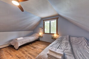 A small, triangular attic bedroom with two single beds, wooden flooring, and a window with a view of trees. - Lakehouse Sleeps 11, Golf, Trails, Lake, Fireplace, True 4-Season (St. Helen)