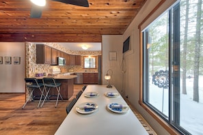 A modern kitchen with wooden ceiling beams, a dining table set with plates, and a view of trees through large windows. - Lakehouse Sleeps 11, Golf, Trails, Lake, Fireplace, True 4-Season (St. Helen)