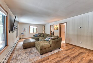 Un salon spacieux avec un canapé d’angle, une grande fenêtre et un plancher en bois.