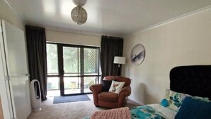 Un dormitorio con cama, una silla, ventilador de techo y un ventanal grande.