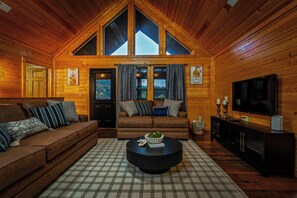 Ein gemütliches Blockhaus-Interieur mit einer braunen Couch, einem runden Couchtisch und einem Fernseher.