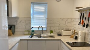 Een moderne keuken met een ingebouwde gootsteen, een raam met zonwering en diverse keukengerei en apparaten.