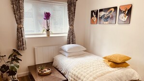 Een slaapkamer met een bed, kussens, een nachtkastje, een potplant, een raam met gordijnen en wanddecoratie.