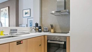A modern kitchen with a stainless steel range hood, a built-in oven, and a white countertop. - Cozy 1-bedroom apartment in Business Bay, Downtown (Dubai)
