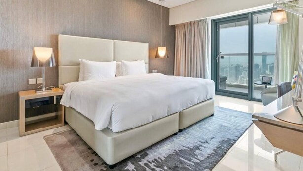 A modern hotel room with a large bed, a desk, and a view of the city through the window. - Cozy 1-bedroom apartment in Business Bay, Downtown (Dubai)