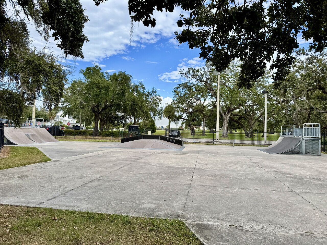 Et tomt skaterpark med betonramper og et fladt område, omgivet af træer og en klar himmel.