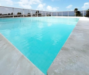 A clear blue swimming pool with a white fence and a sky with clouds. - Puerto Ventura By Day by Day (João Pessoa)