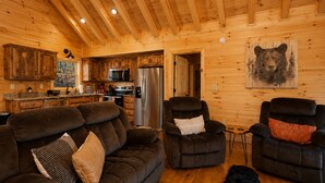 A cozy cabin interior with a wooden interior, a sofa, two recliners, a refrigerator, and a bear painting on the wall. - Romantic Log Cabin • Hot Tub + Vinyl Records • 15 Min to Ellijay (Ellijay)
