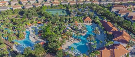 An aerial view of a residential area with a large swimming pool surrounded by palm trees and a gazebo.
