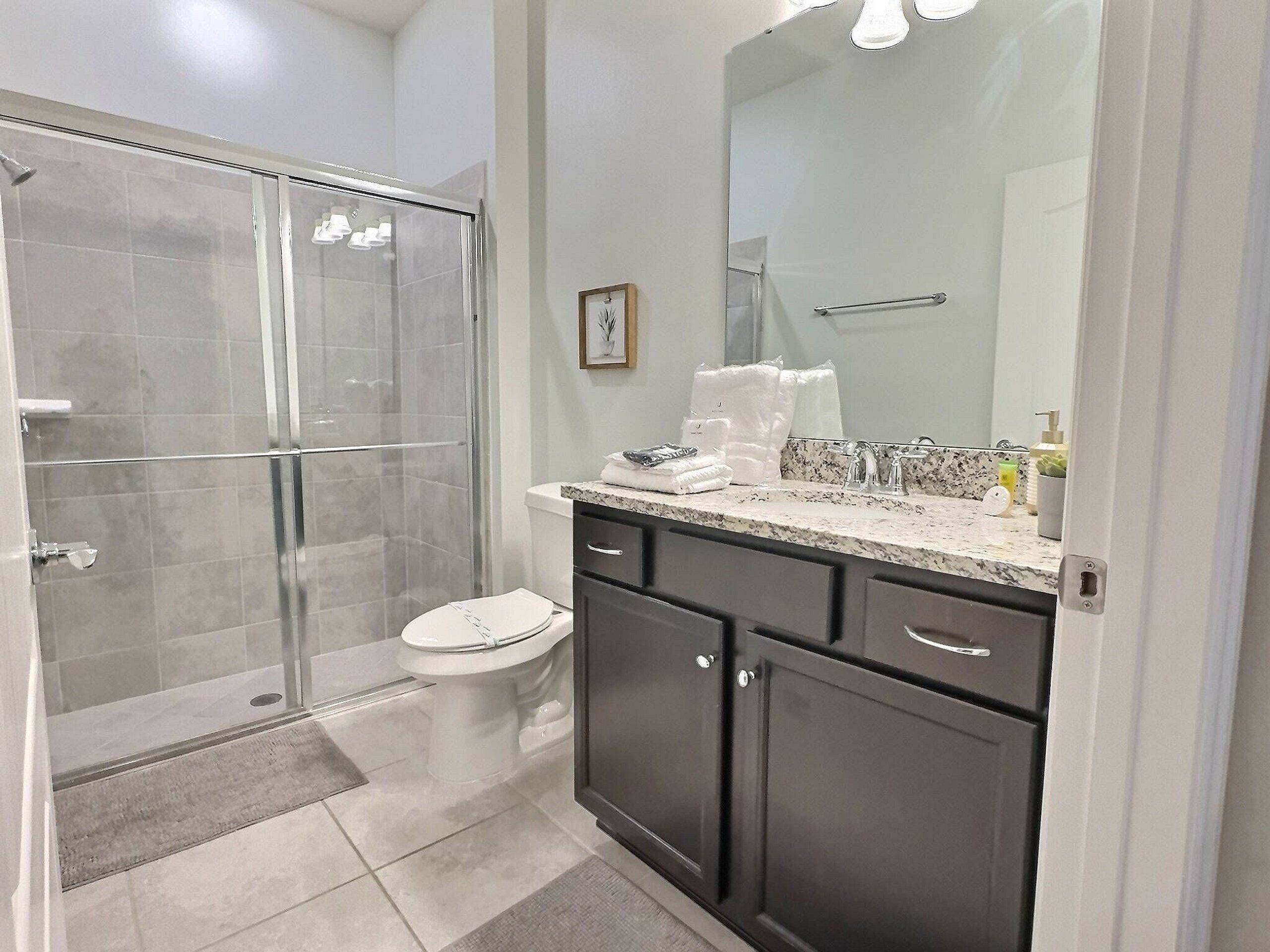 A modern bathroom with a glass-enclosed shower, a white toilet, dark cabinets, and a marble countertop.