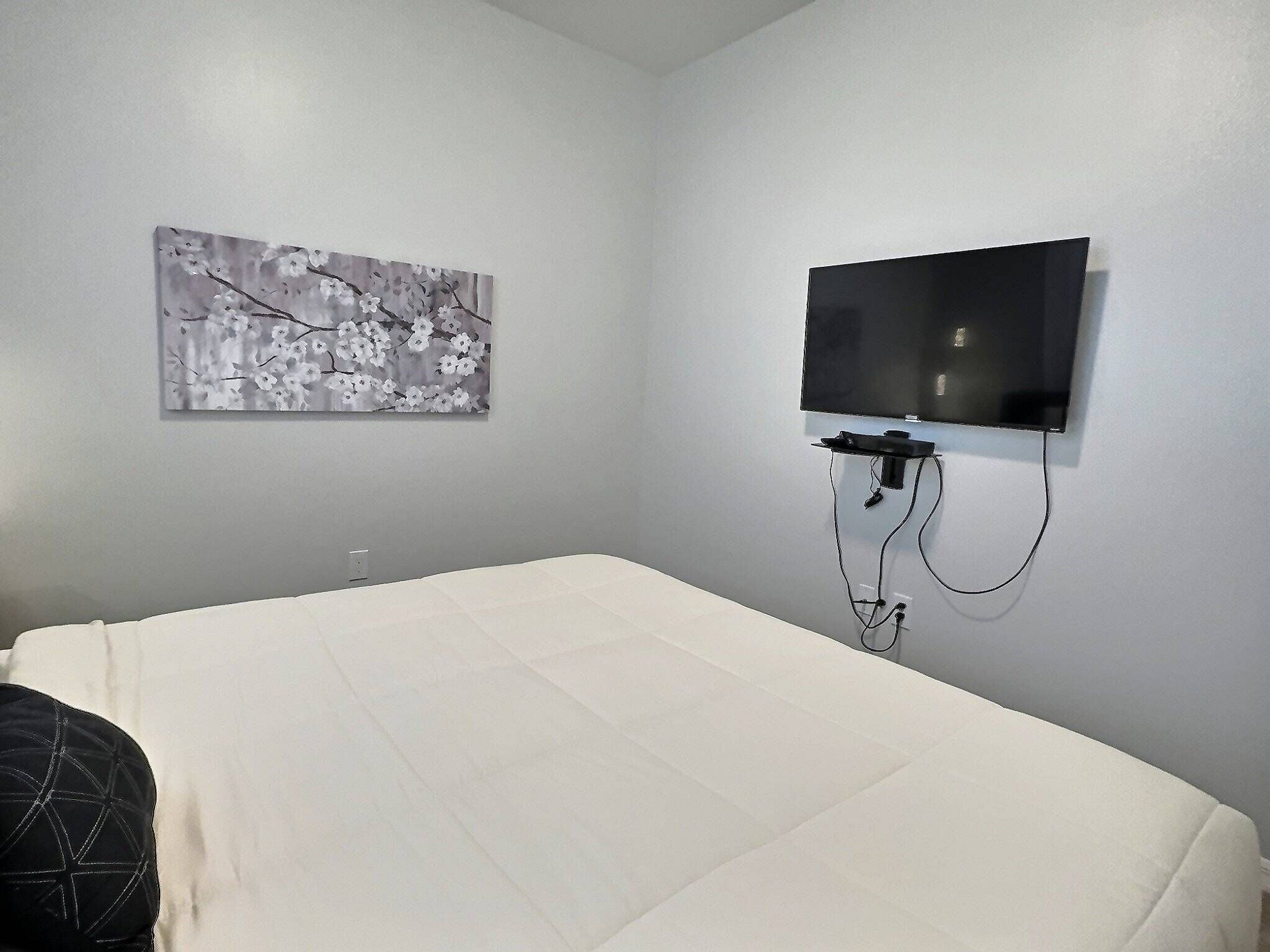 Un dormitorio con una cama, un televisor montado y una obra de arte en la pared.