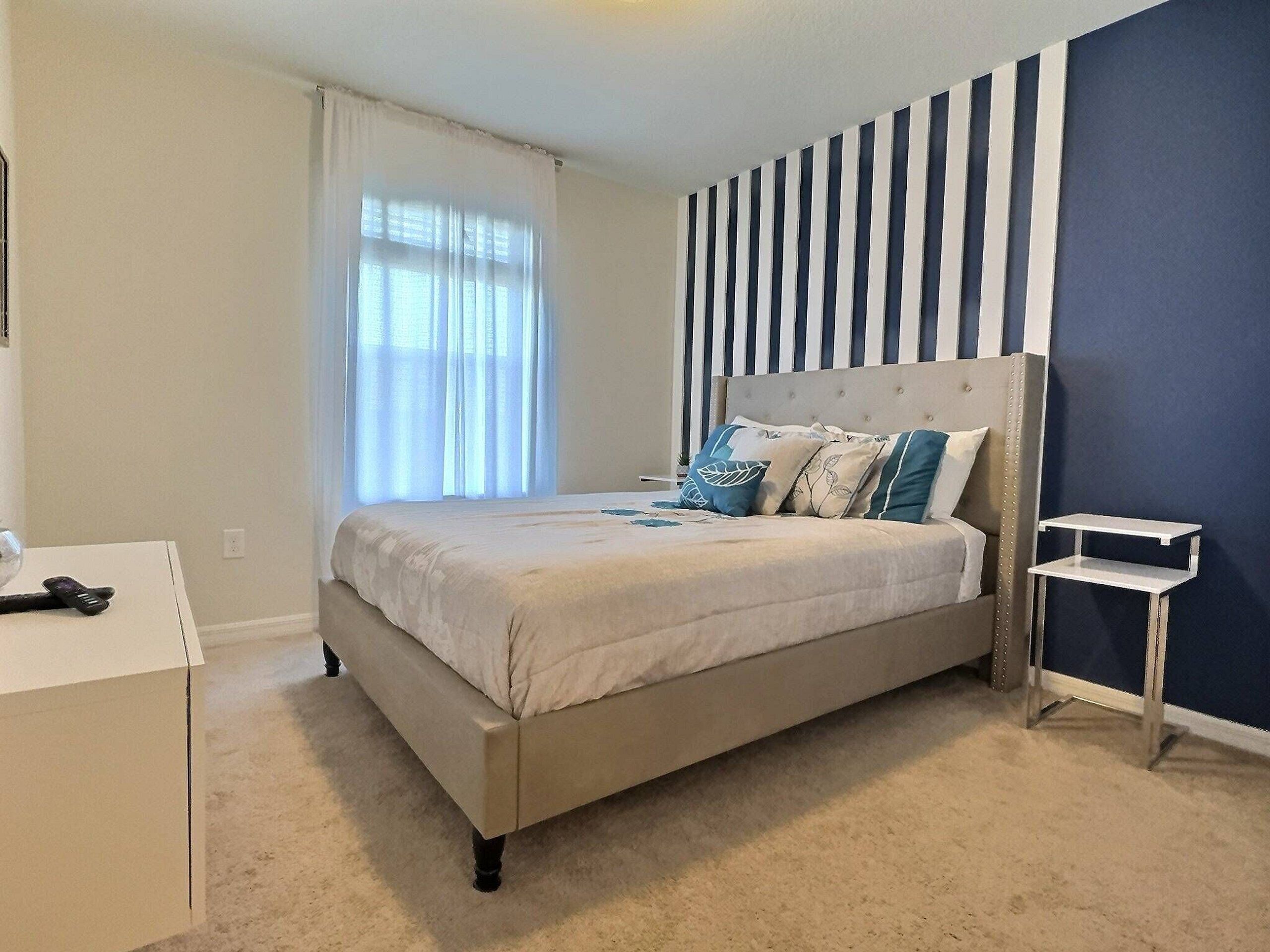 Un dormitorio con cama, mesita de noche y ventana con cortinas.