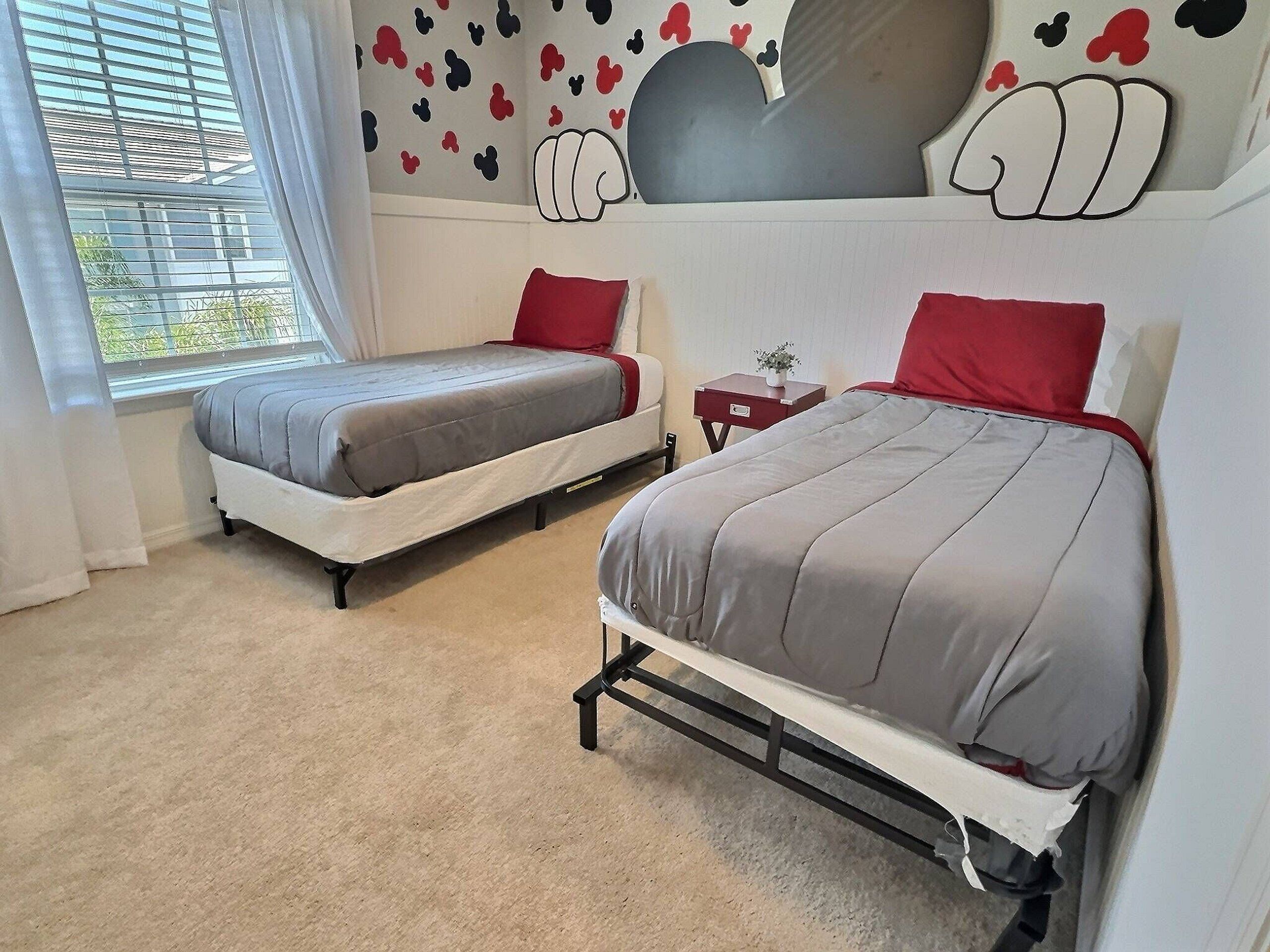 A bedroom with two beds, a window, and a wall with a cartoon character design.