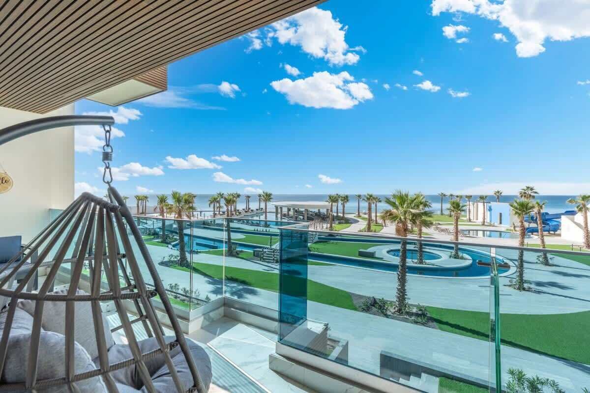 Un balcone con vista su una zona piscina, palme e cielo sereno.