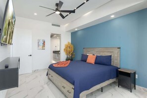 A bedroom with a bed, a desk, a ceiling fan, and a nightstand.