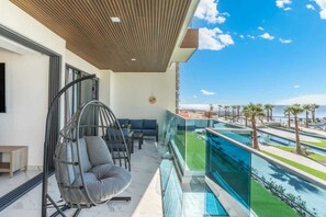 A balcony with a hanging chair, a sofa, and a view of a pool and palm trees.