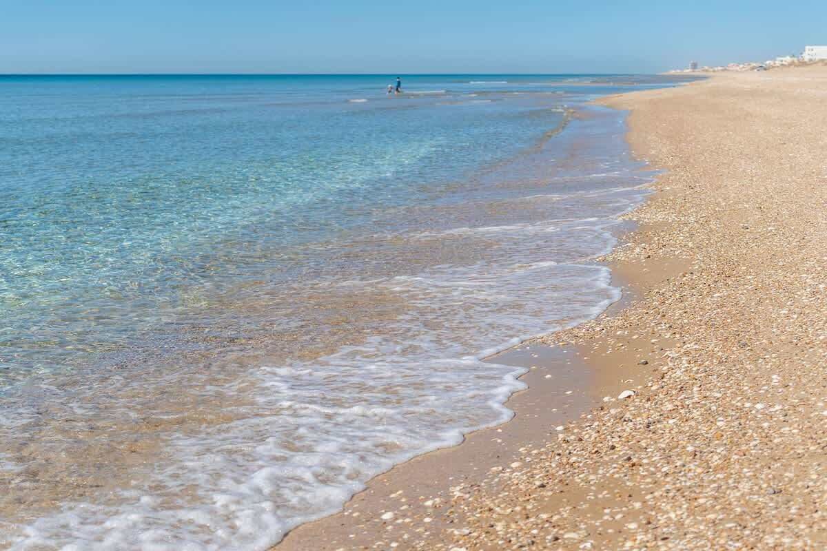 Ein Strand mit klarem Wasser, Kieselsteinen und einer entfernten Küste.