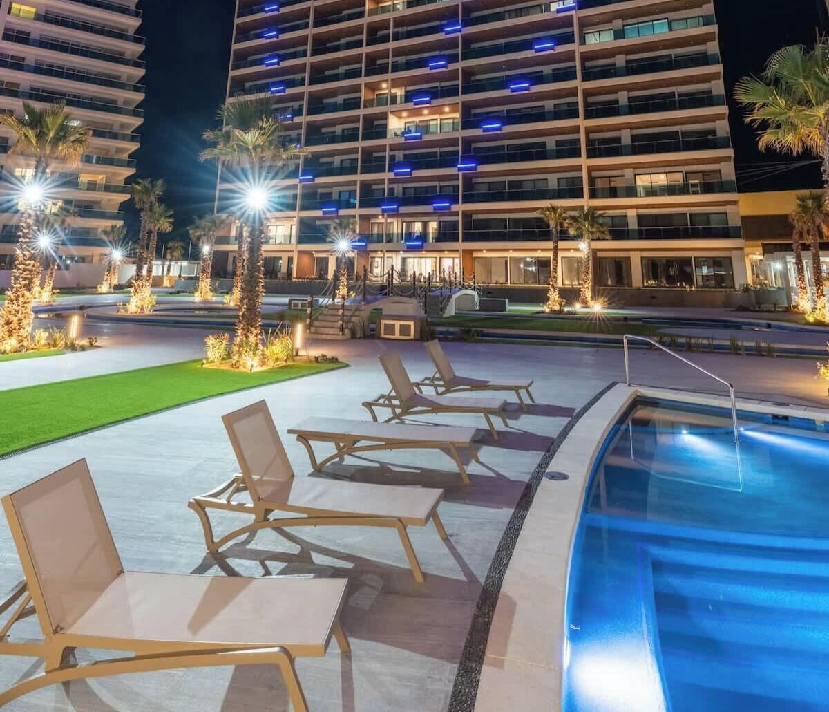 Un espace piscine d’hôtel avec des chaises longues et une piscine illuminée la nuit.