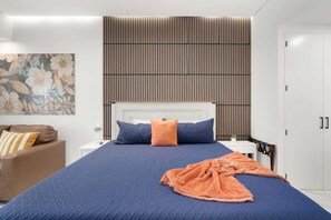 Ein modernes Schlafzimmer mit einem großen Bett, einem Nachttisch, einem Sessel, einer Wandtafel und einer Tür.