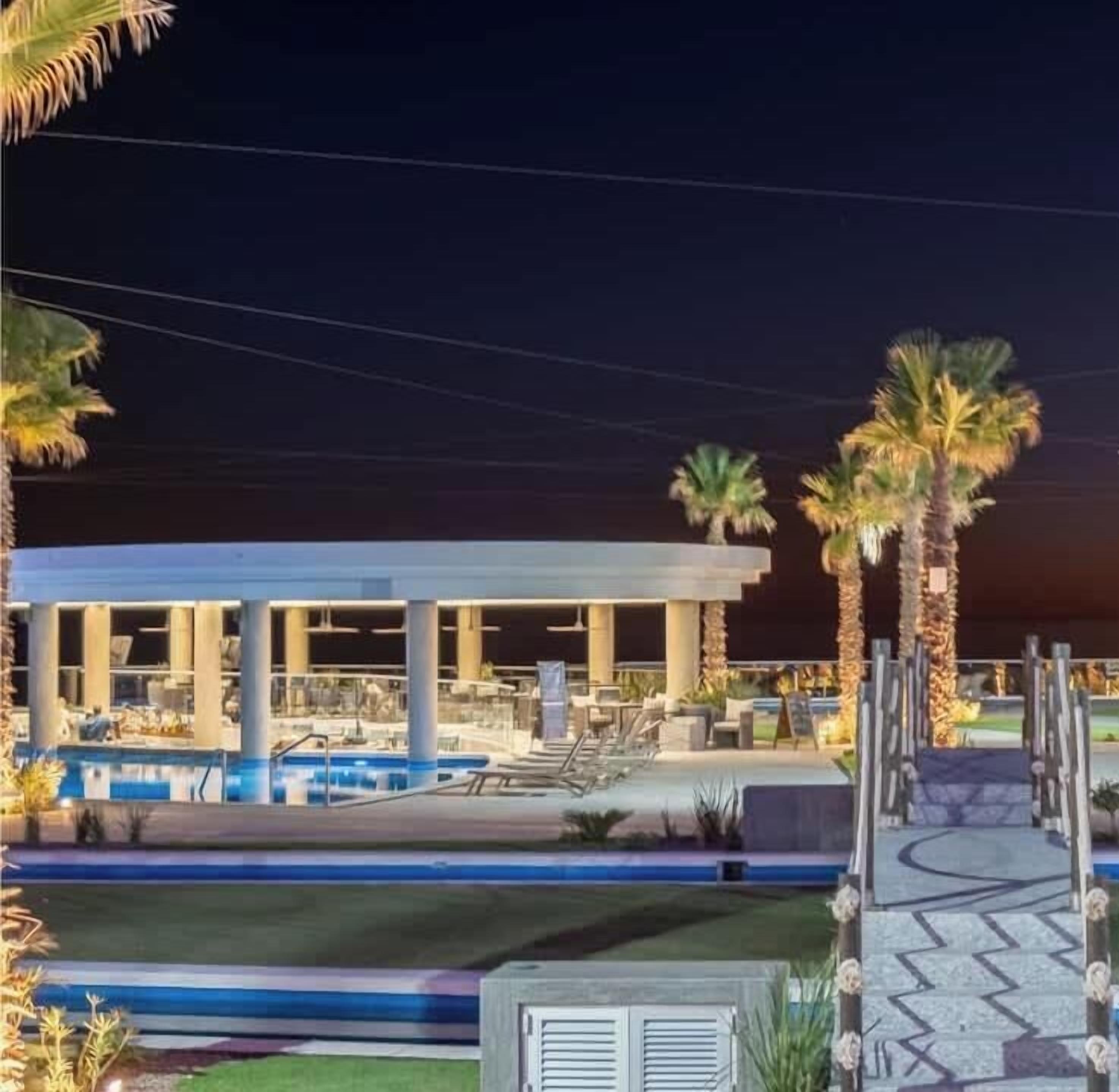 A resort with a pool, palm trees, and a covered area.