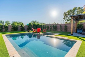 A rectangular swimming pool with a clear blue surface, surrounded by a well-maintained lawn and a low brick wall. - The One | Glendale | Pool & Spa | State Farm (Glendale)