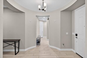 A hallway with a white door at the end, a black table on the left, and a white door on the right. - The One | Glendale | Pool & Spa | State Farm (Glendale)