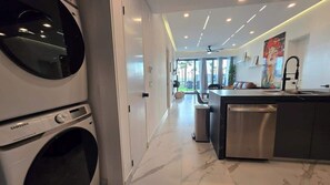 A modern kitchen with a built-in dishwasher, a dining area with a view, and a laundry area with a Samsung washing machine.