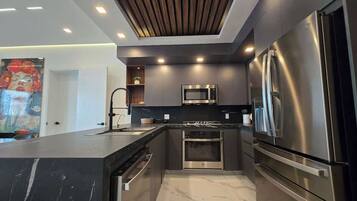 Een moderne keuken met een centraal eiland, roestvrijstalen apparatuur en een houten plafond.