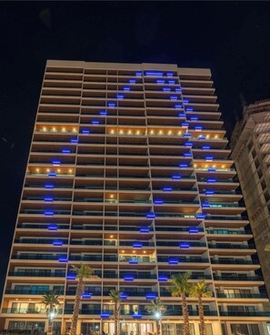 Een meerlaags hotel met een modern ontwerp, met balkons en een opvallend lichtpatroon op de gevel.