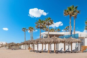 Ein Strand mit Palmen, Liegestühlen und Reetdachschirmen.