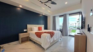 A modern hotel room with a large bed, a nightstand, a TV, and a balcony with a view of the ocean.