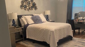 Una camera da letto con un letto, comodini, una scrivania, una sedia, un lampadario e una finestra con persiane.