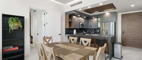 A modern kitchen with a dining area, featuring a central island, built-in appliances, and a bookshelf with decorative items.