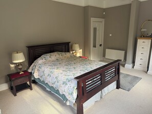 A bedroom with a bed, nightstands, a dresser, a door, and a radiator.