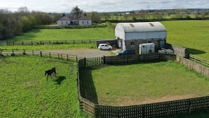 A rural property with a fenced pasture, a white house, and a large barn.
