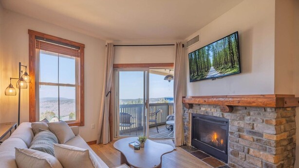 A cozy living room with a fireplace, a sofa, a coffee table, and a large TV mounted on the wall. - Mountain Soul Retreat (Snowshoe)
