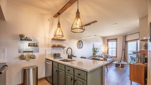 A modern kitchen with a central island, pendant lighting, and a dining area with a sofa and coffee table. - Mountain Soul Retreat (Snowshoe)