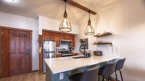 A kitchen with wooden cabinets, stainless steel appliances, a white island with bar stools, and pendant lighting. - Mountain Soul Retreat (Snowshoe)