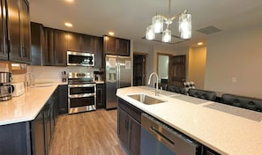 A modern kitchen with dark wood cabinets, stainless steel appliances, a large island with a sink, and a unique light fixture. - Keystone Lodge A | Ski-In/Out, Hot Tub! (Snowshoe)