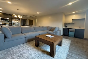 A modern living room with a sectional sofa, a wooden coffee table, and a kitchen area with a refrigerator and oven. - Keystone Lodge A | Ski-In/Out, Hot Tub! (Snowshoe)