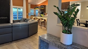Ein modernes Wohnzimmer mit einem grauen Ecksofa, einem Essbereich mit weißem Tisch und Stühlen sowie einer Küche im Hintergrund.